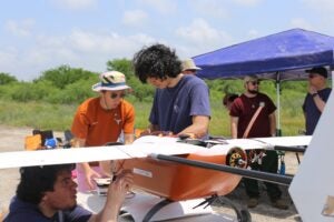 Three students work on orange drone