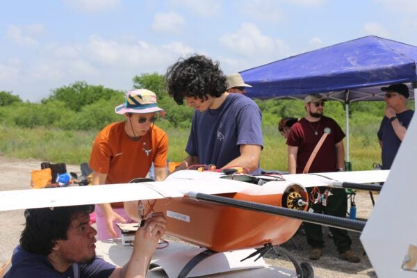 Three students work on orange drone