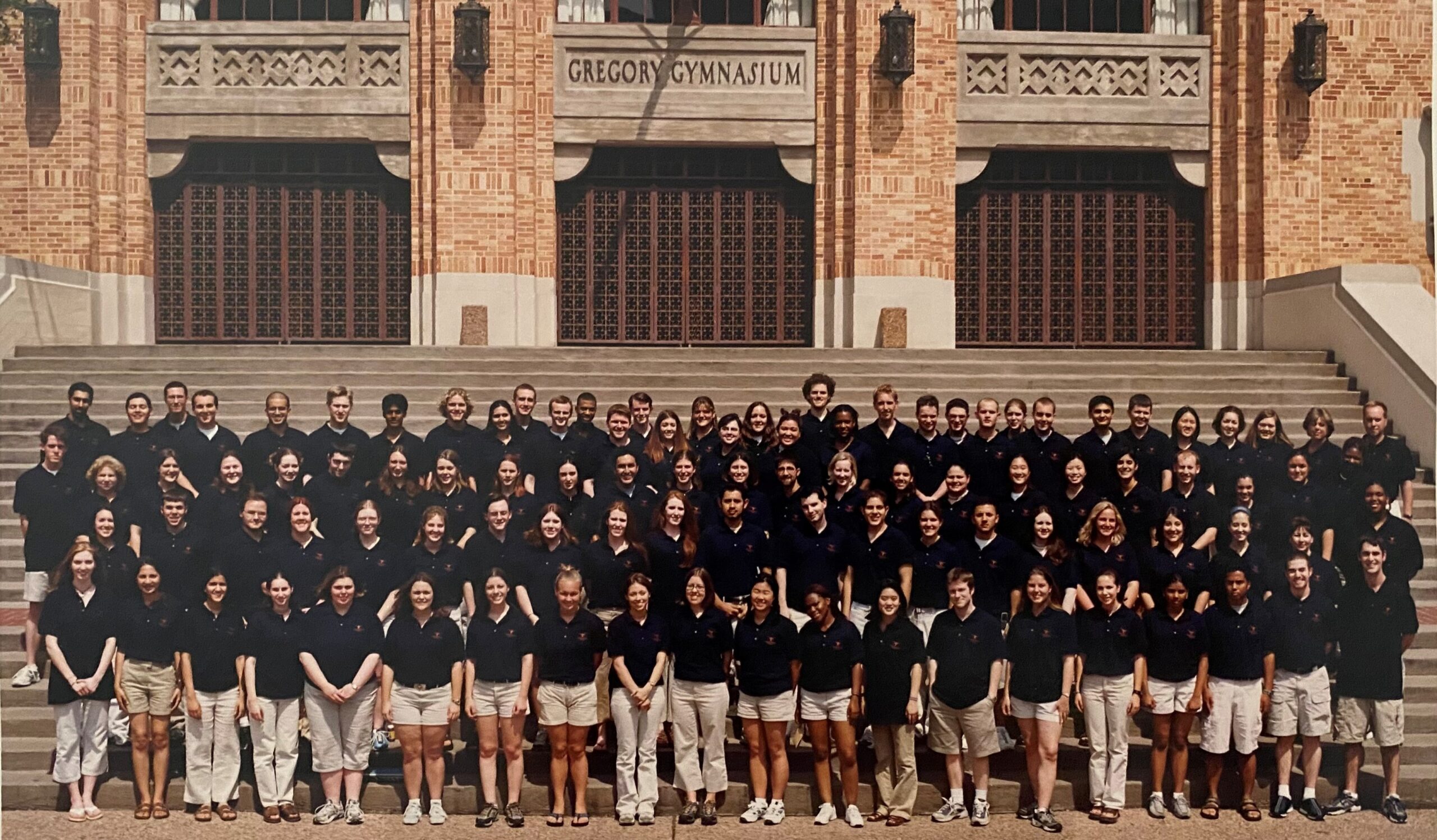 Students in black polos and khaki shorts stand in front of Gregory Gymnasium