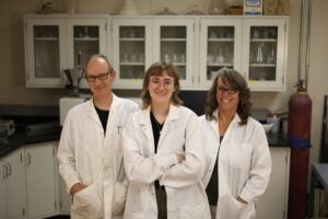 Three people stand together wearing white lab coats