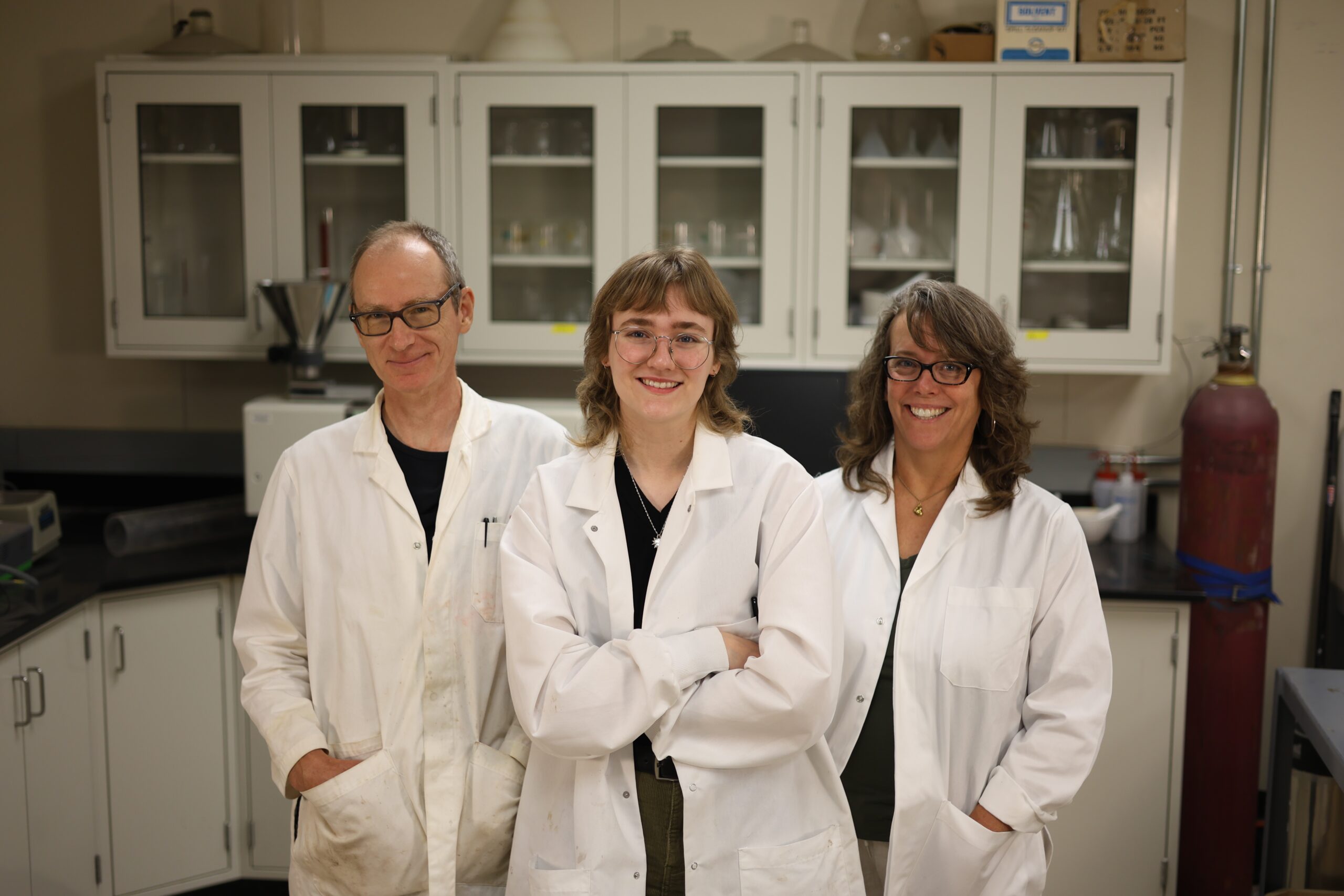 Three people stand together wearing white lab coats