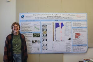 Student stands in front of research poster.