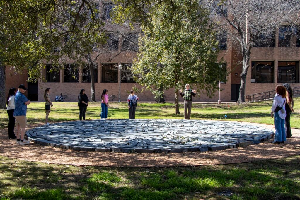 People stand around an outdoor circular artwork on the ground