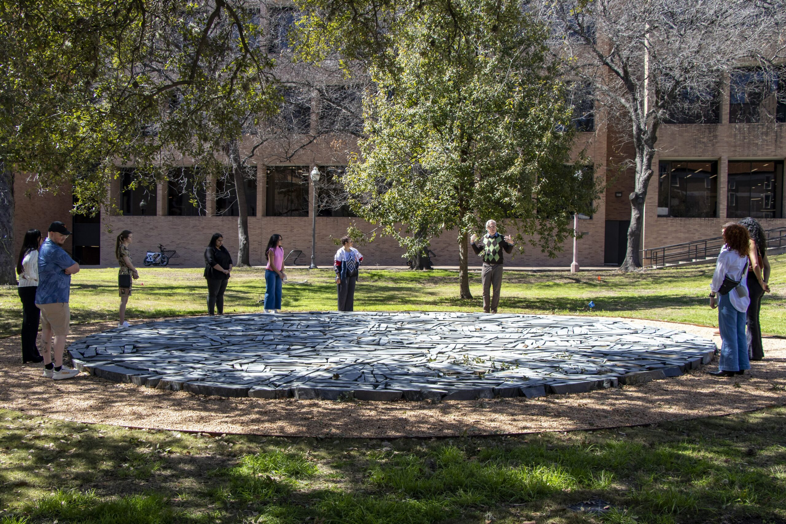 People stand around an outdoor circular artwork on the ground