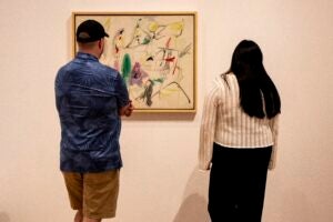 Two students stand with their backs to camera, looking at a painting