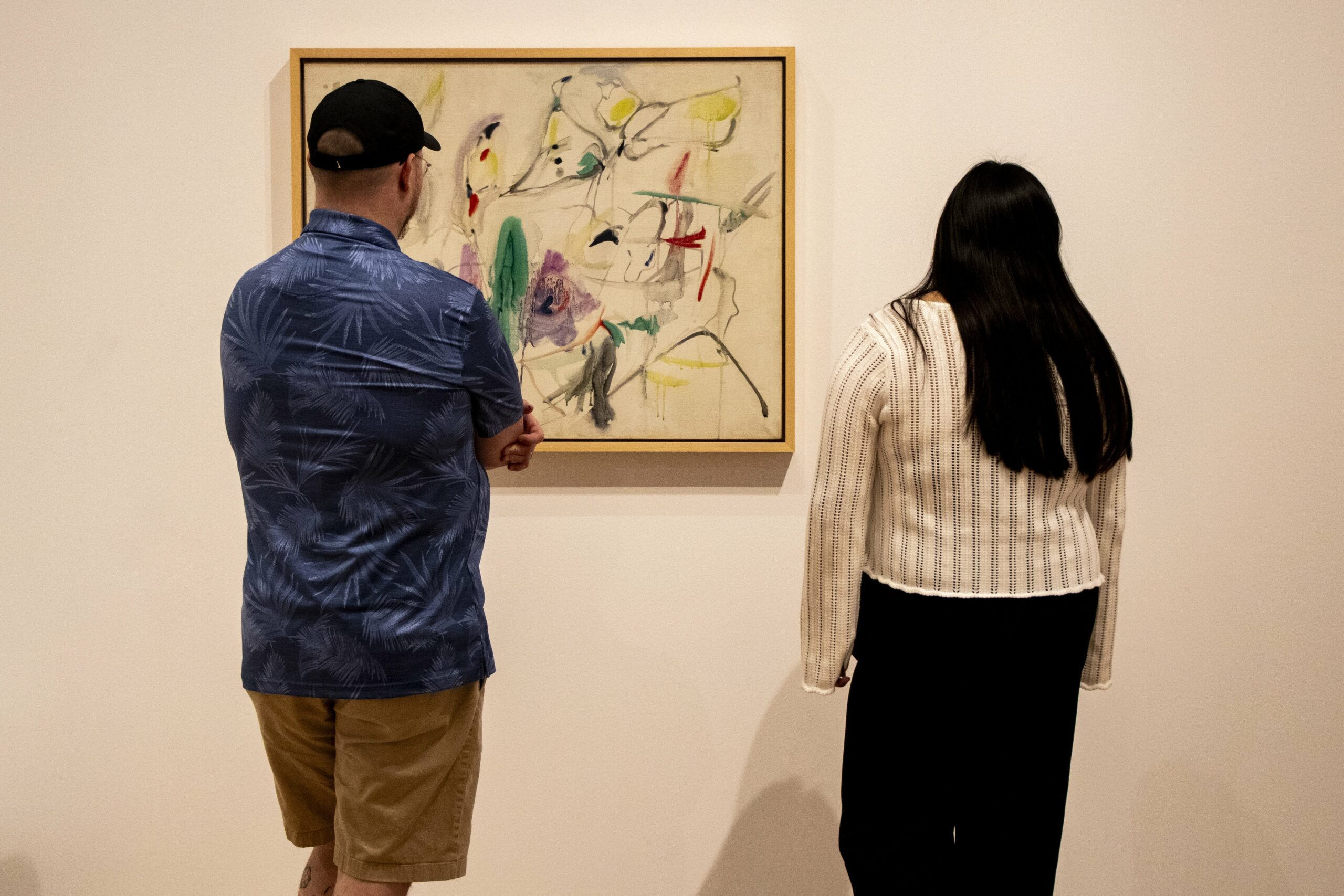 Two students stand with their backs to camera, looking at a painting