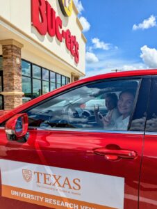 Two women sit in red car in front of Buc-ee's