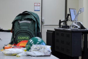 Emergency supplies laid out on a table in front of a green backpack.