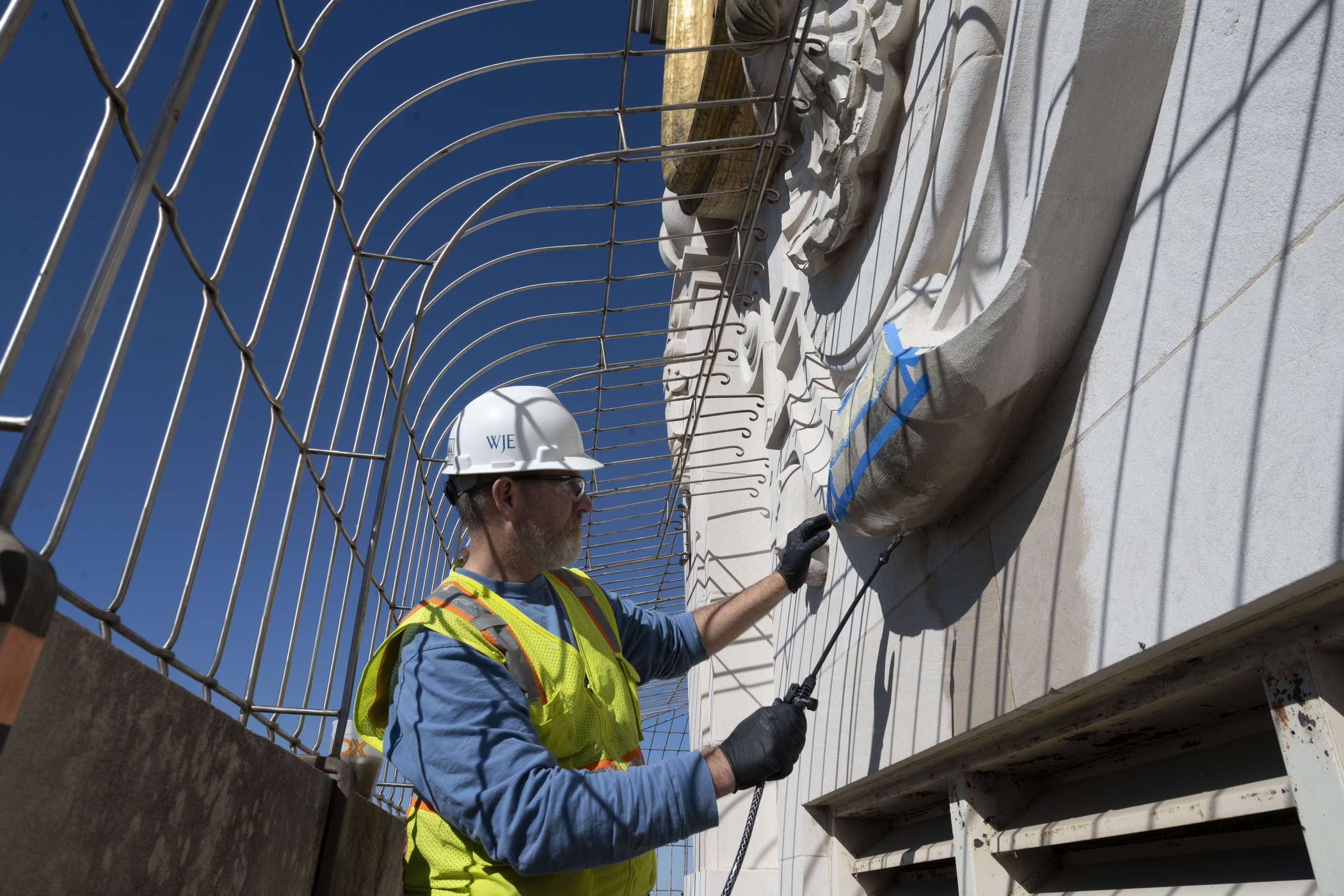 Man in hardhat cleans stonework below clock with sprayer