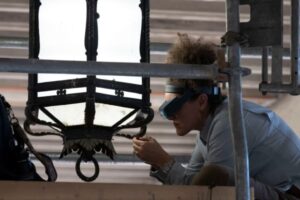 Woman on scaffold examines lantern on loggia