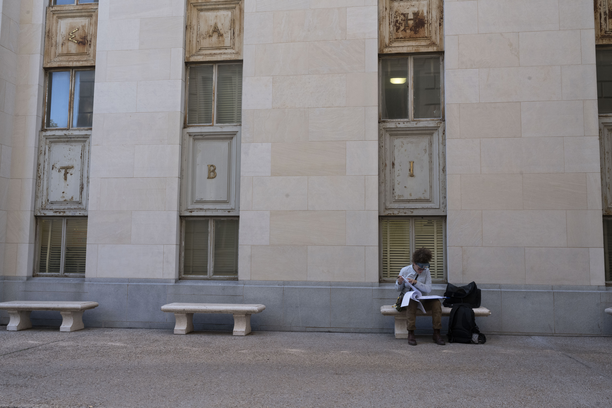 woman sits on bench in courtyard and studies papers