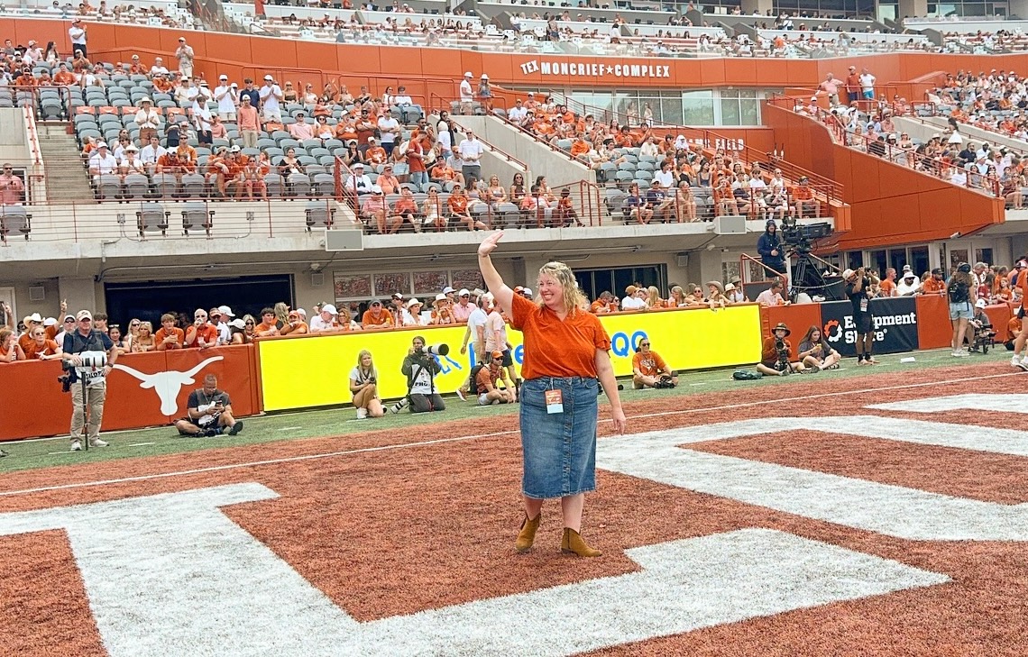 Woman waves to crowd at Texas Football game.
