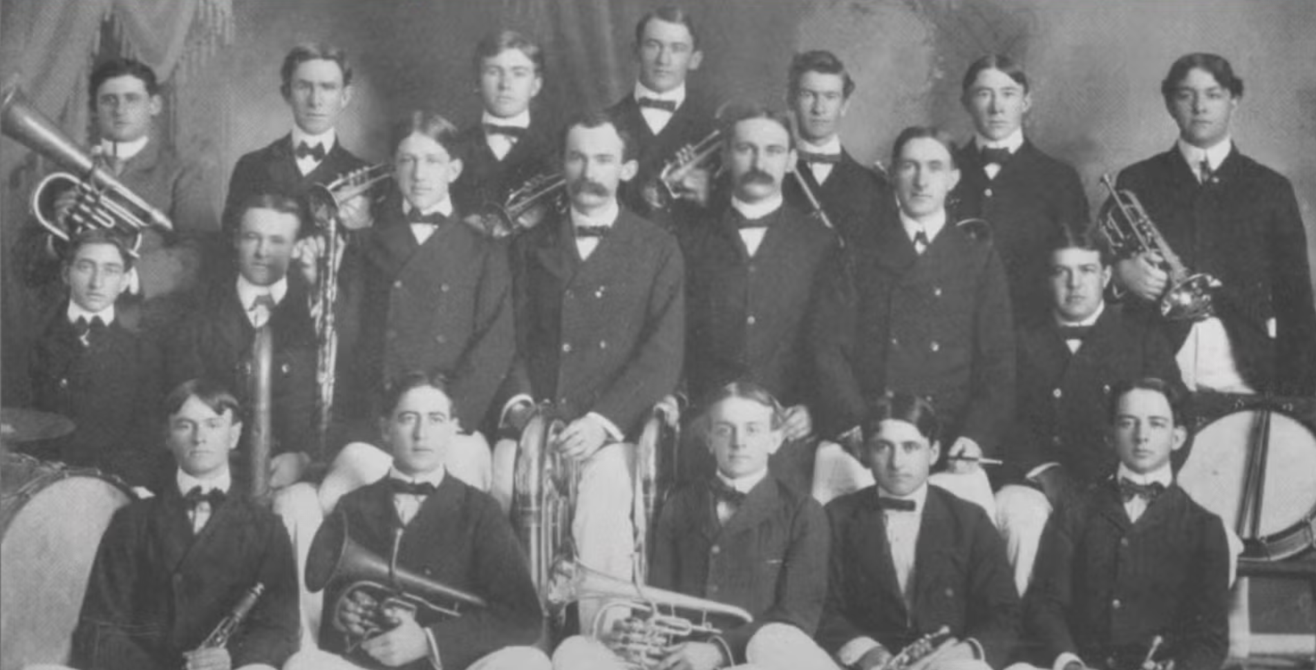 An antique photo of 19 young men with horns wearing bow ties