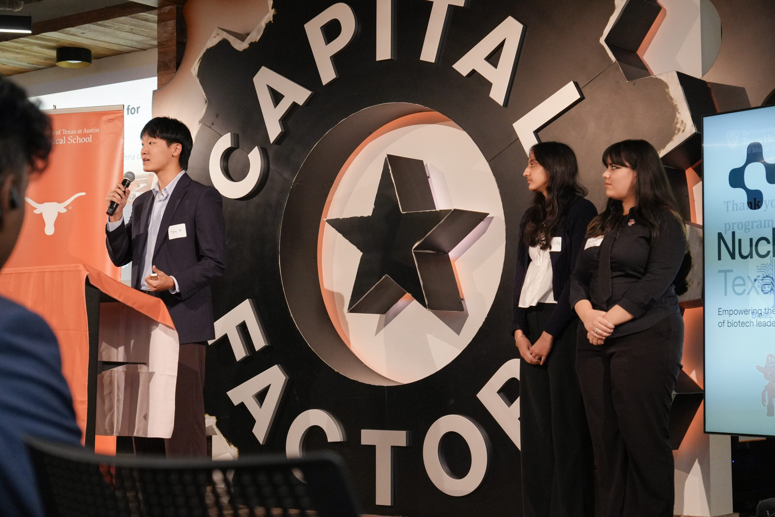 Three people stand in front of Capital Factory sign.