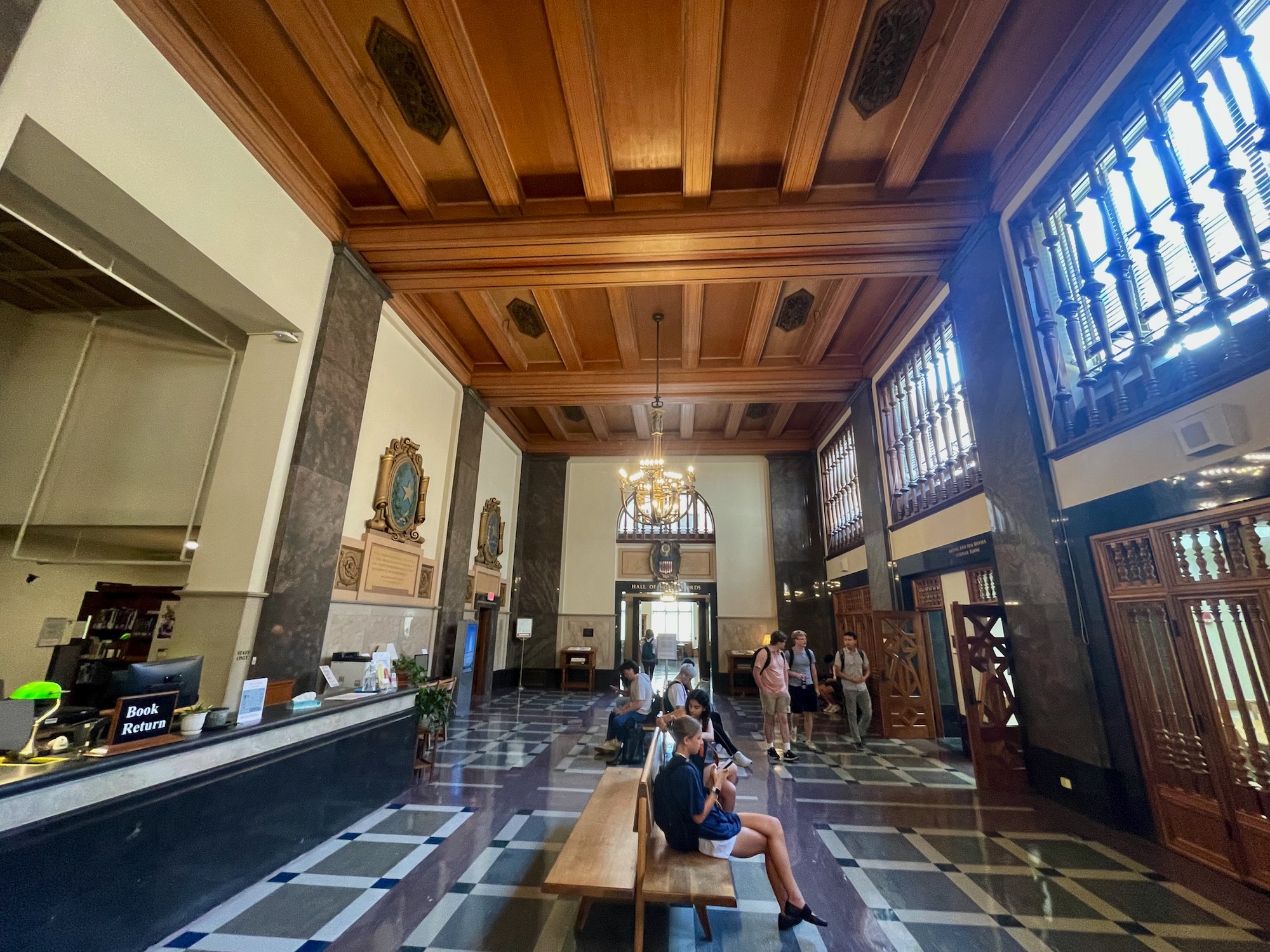 high-ceilinged room with wooden beams and students walking. and sitting