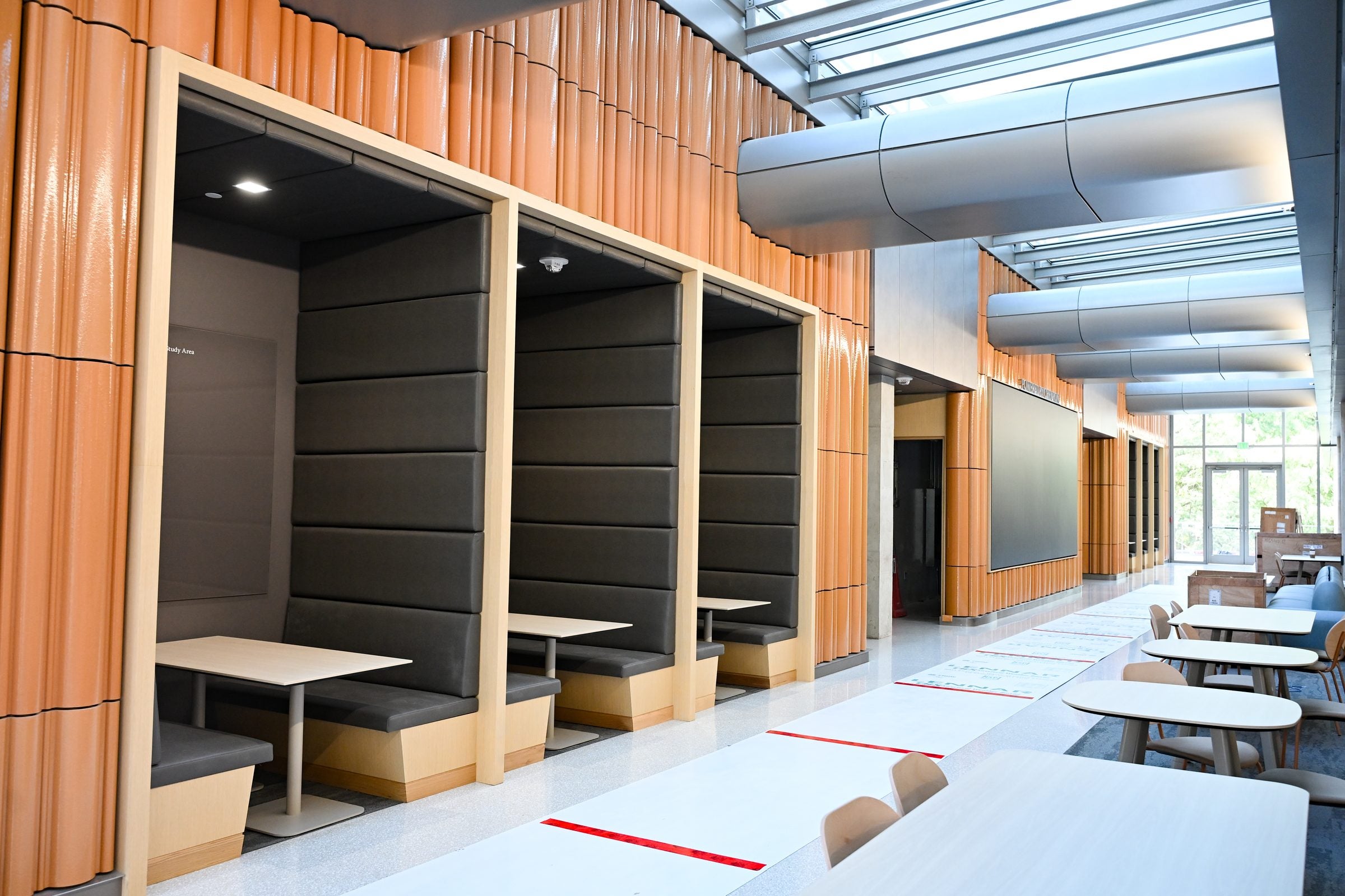 Room with tables, chairs and booths with orange walls.