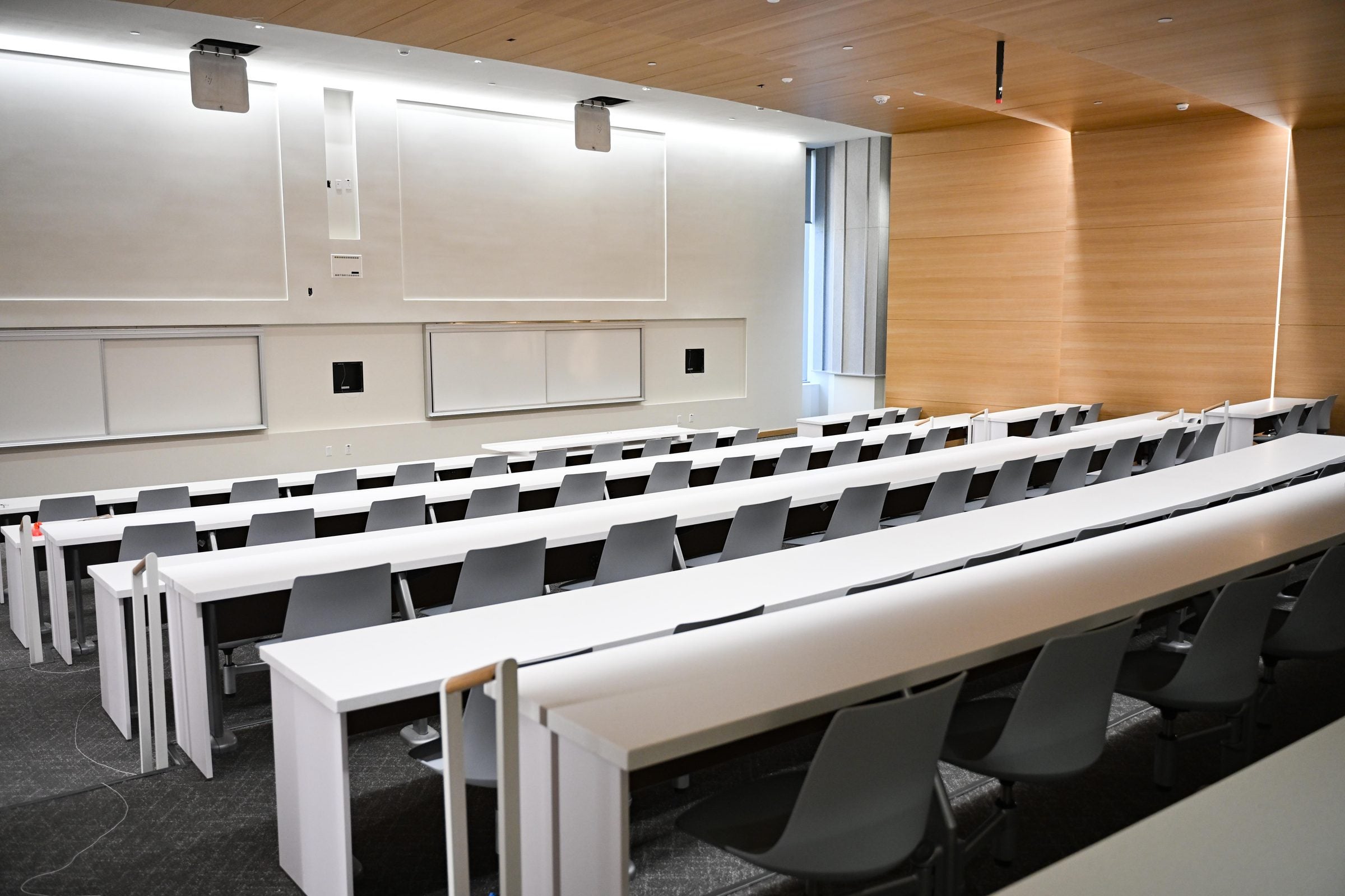 Lecture hall with rows of long white tables and grey chairs.