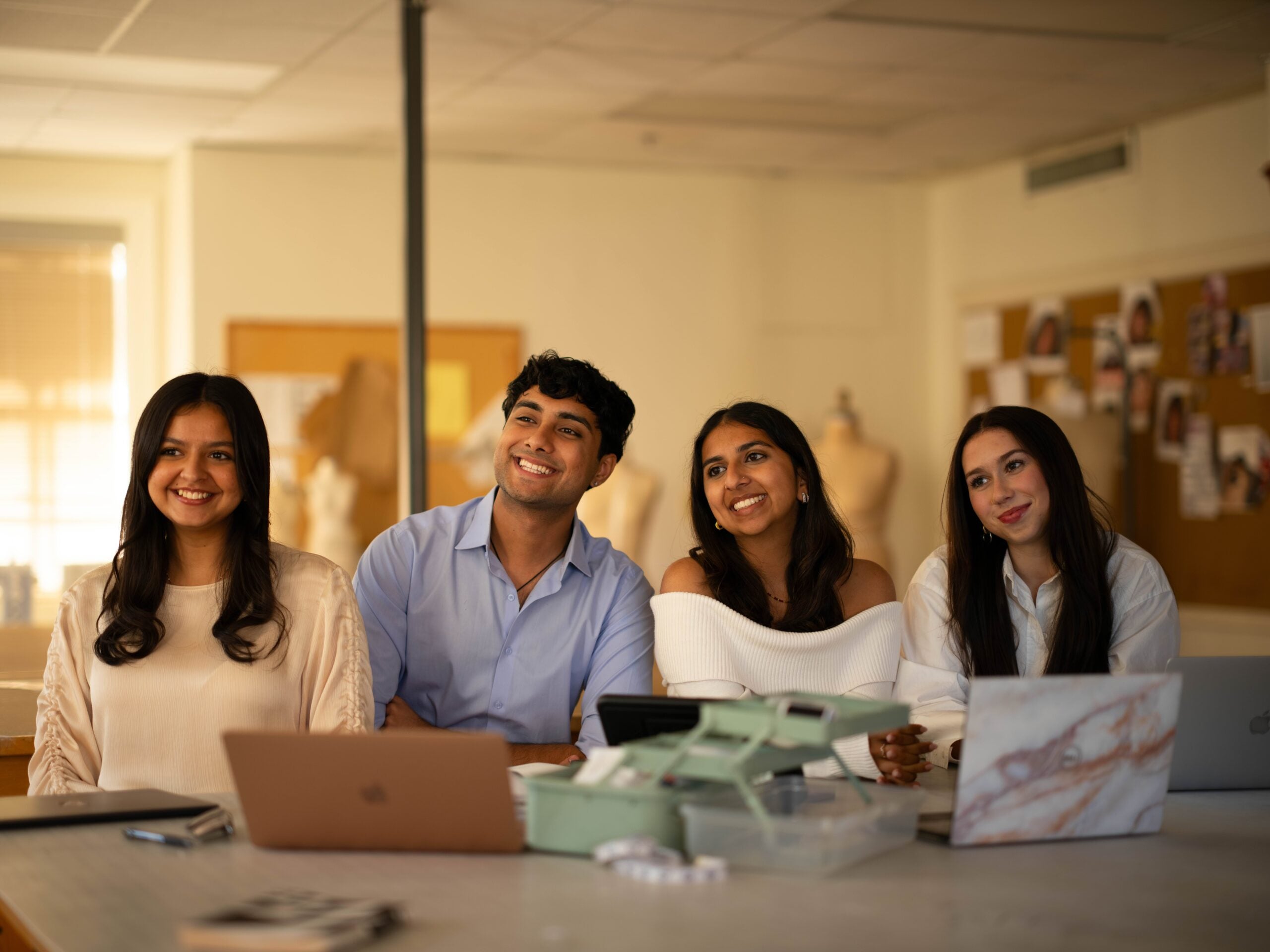 Image of four students sitting at a table smiling, laptops in front of them
