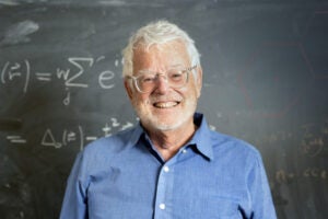 Man smiles in front of equation on chalk board