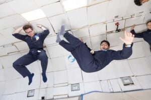 Two people midair in blue coveralls in white tunnel.