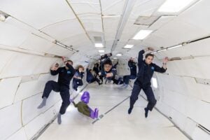 People midair in blue coveralls in white tunnel.