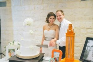 Bride and husband stand next to white take and orange Tower cake