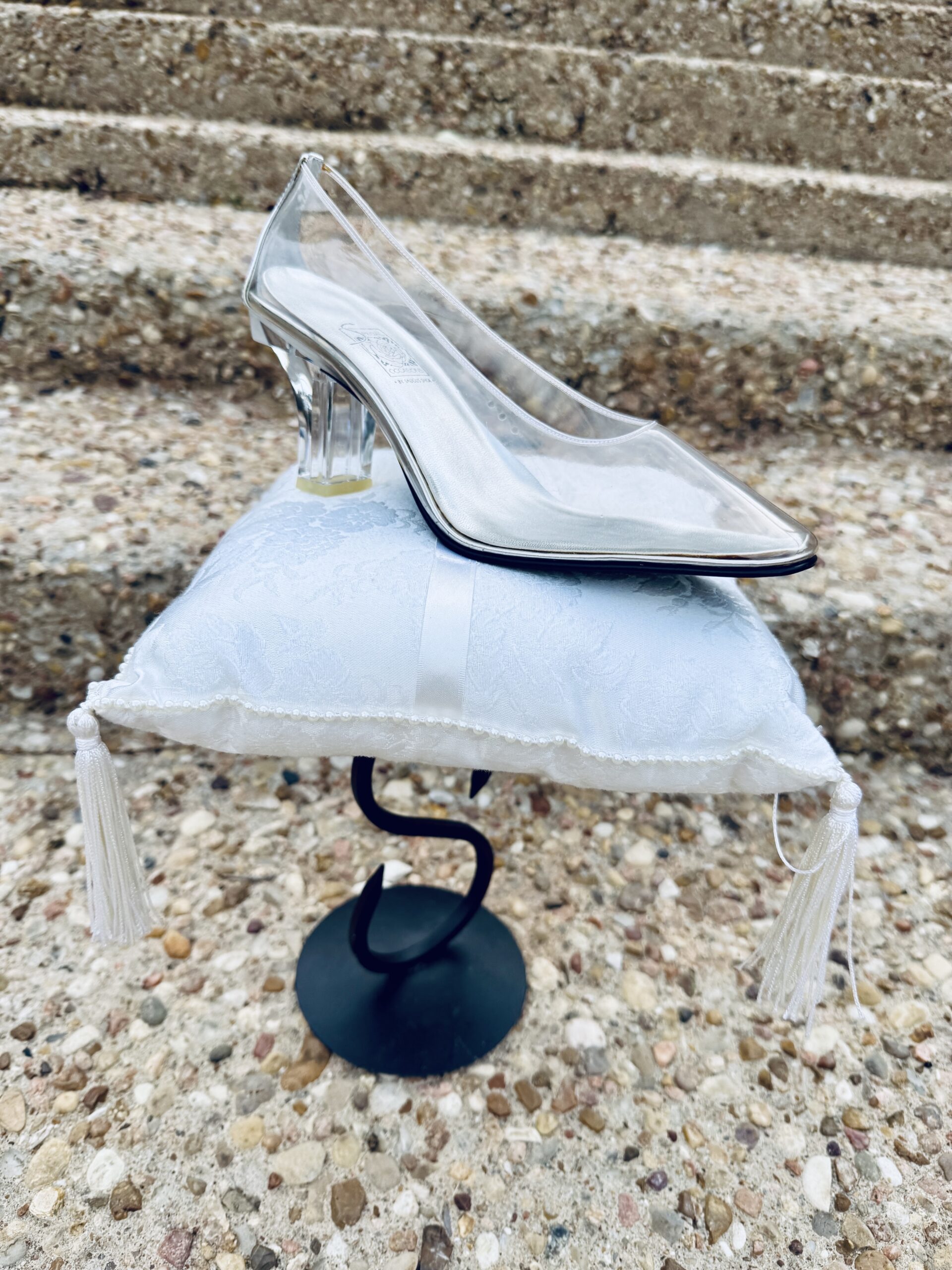 A glass slipper rests on a pillow in front of a staircase.