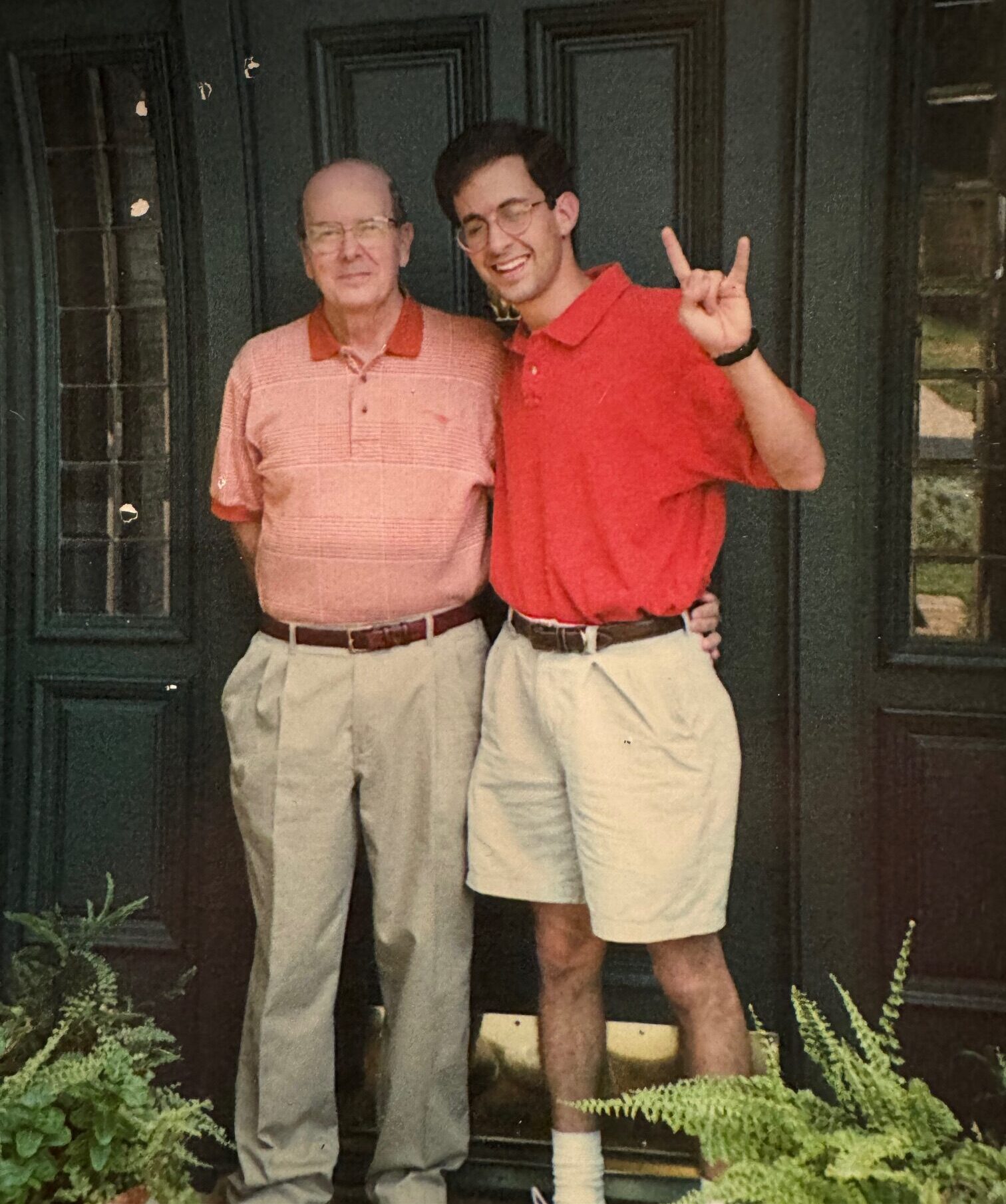 A father and his adult son pose for a photo; the son holds up the Hook 'em, Horns hand sign.
