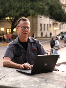 Man sits with computer near UT Tower