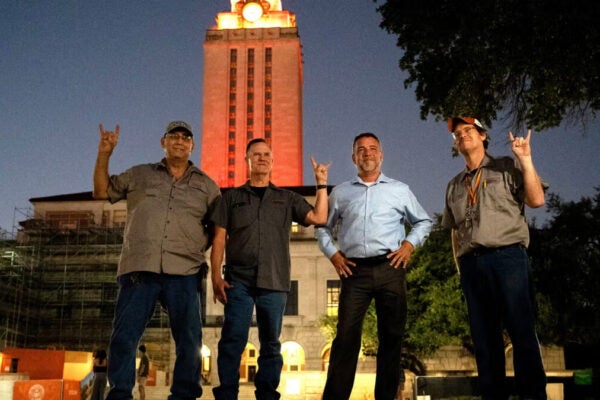 four men stand in front of lit UT Tower at night