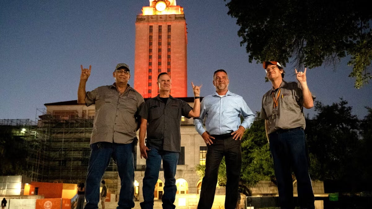 four men stand in front of lit UT Tower at night