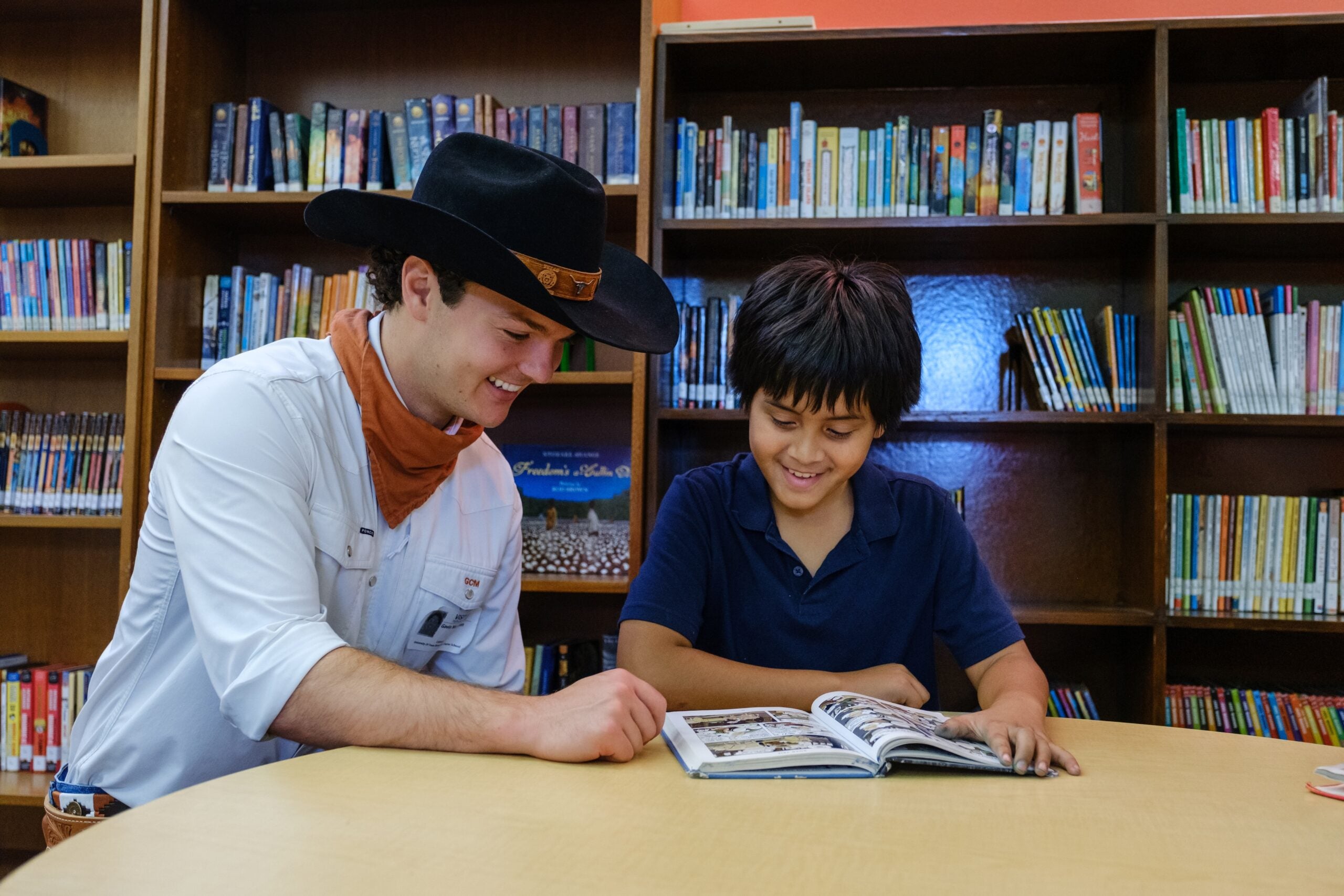 College student and elementary student read together in library.