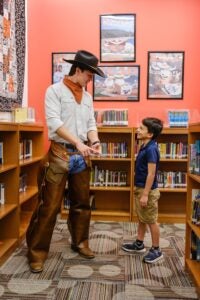 College student and elementary student stand talking in library.