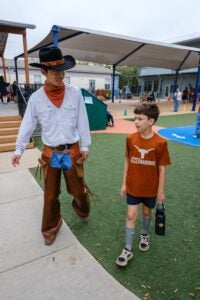 College student and elementary student walk together on elementary playground.