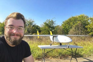 a student taking a selfie with a small aircraft sitting on a table