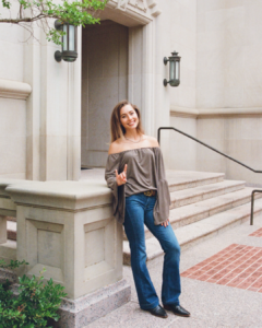 image of a woman leaning against a building holding up hook 'em
