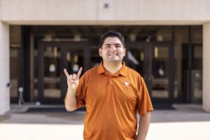 man in orange polo stands in front of UT building