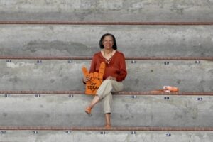 Woman sits alone on concrete bleachers holding a large foam Hookem hand