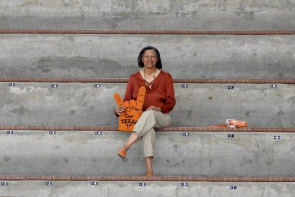 Woman sits alone on concrete bleachers holding a large foam Hookem hand