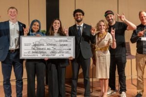 image of students with a check for their winning presentation alongside judge panel