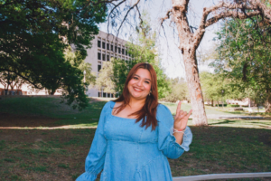 image of a woman standing in front of trees and buildings holding up hook 'em