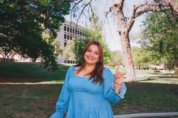 image of a woman standing in front of trees and buildings holding up hook 'em