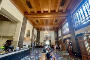 Hall of the Six Coats of Arms, high walnut-paneled ceiling, high windows on the right, students sitting and walking, ornate linoleum floor
