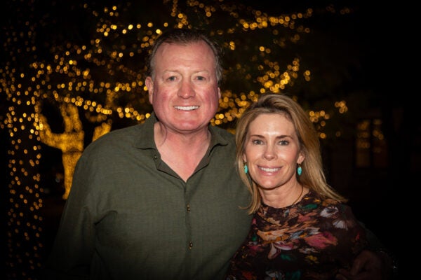 Married couple poses for a photo at night in front of holiday lights on trees.