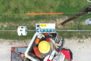 Utility worker in a vest and hard hat attaches a blue sensor to a power line.