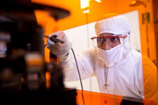 Student dressed in white safety coveralls and goggles works in a lab.