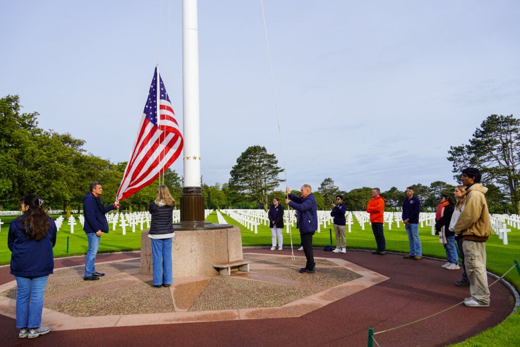 image of a group of people raising an American flag over the Normandy American Cemetery