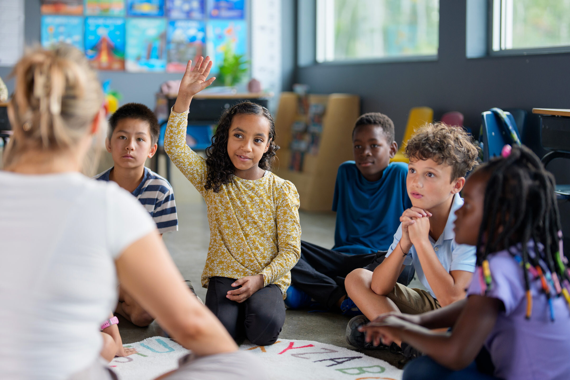 Children sit on the ground in front of their teacher in a classroom