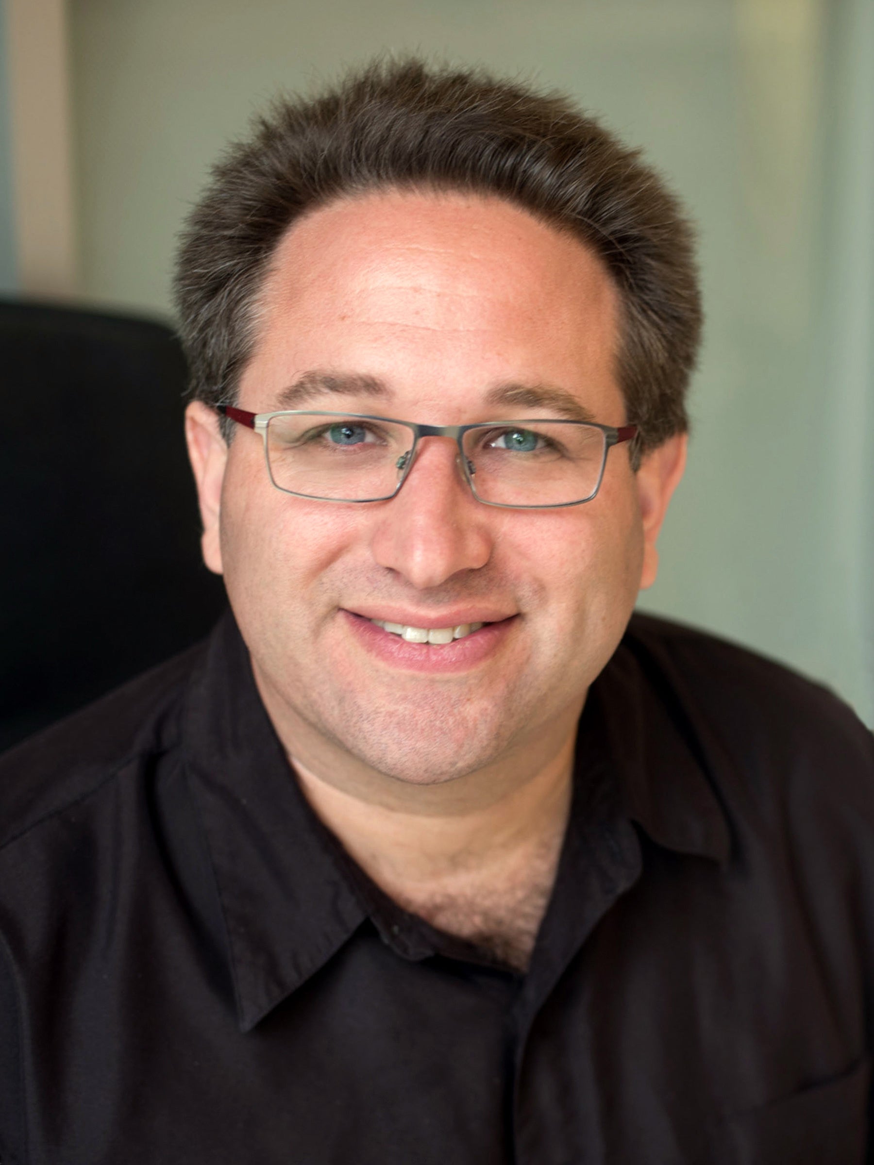 A portrait of a man wearing glasses and a black shirt.