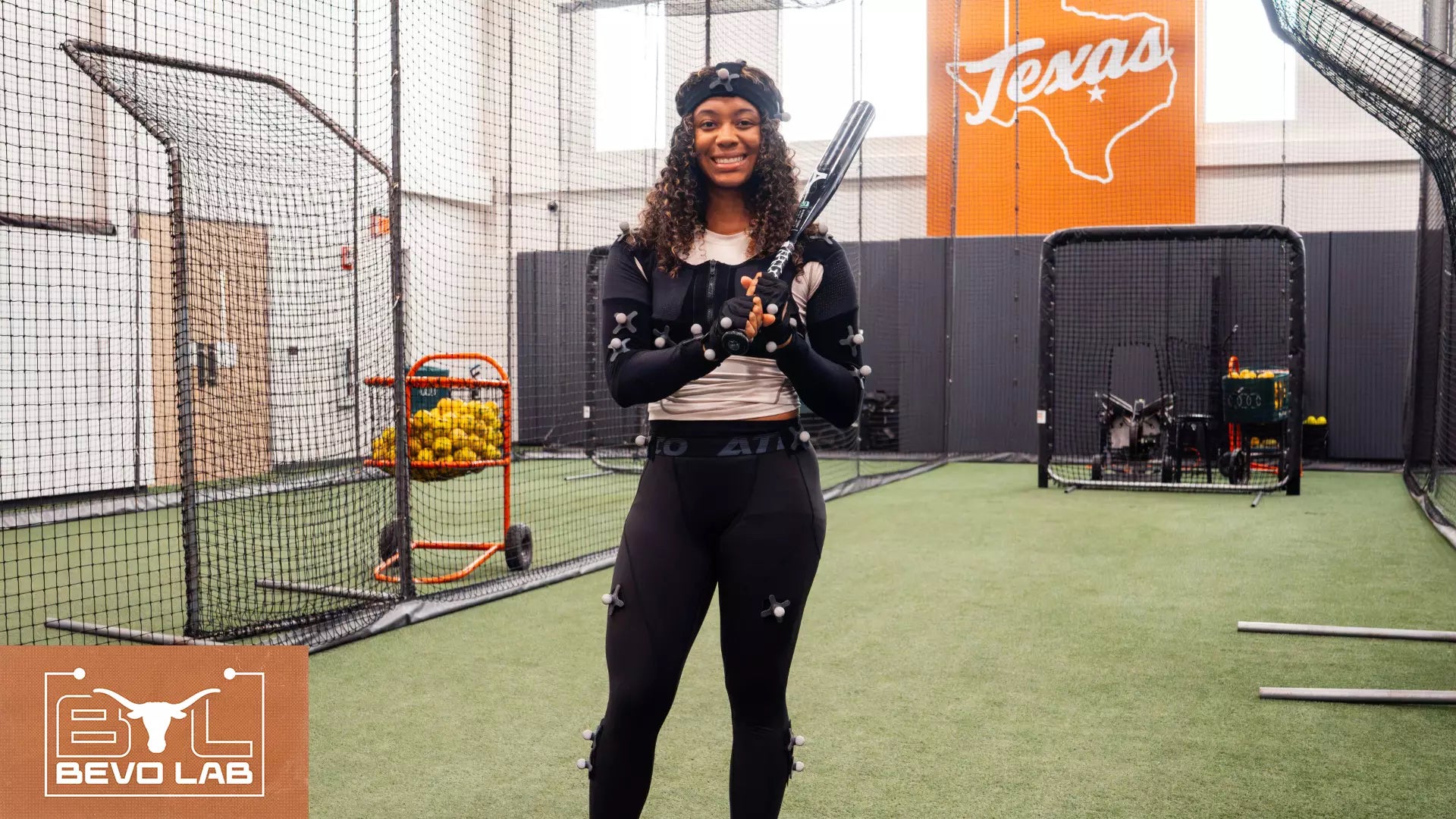 Woman stands in a batting cage with a baseball bat